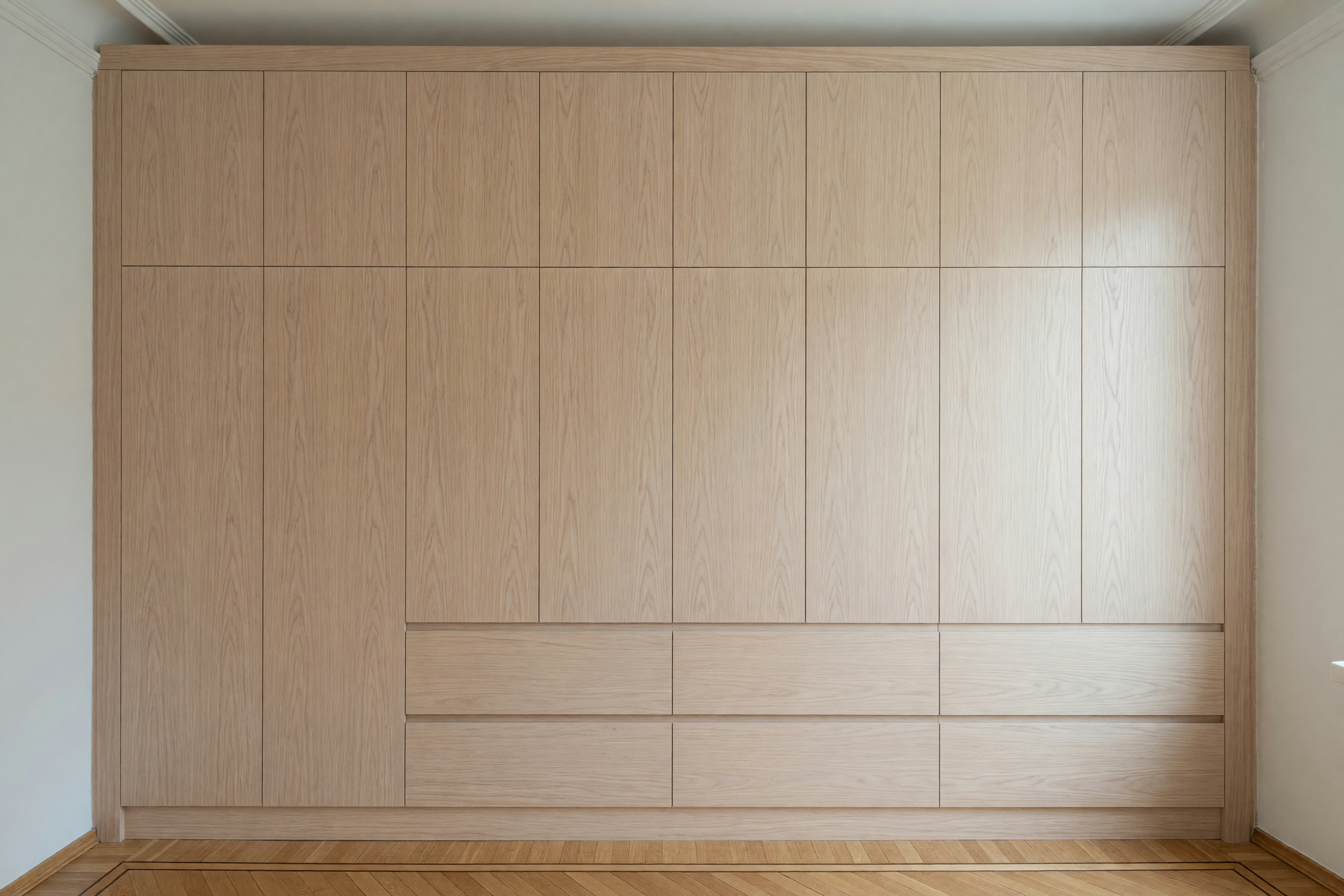 Raumhohe maßgefertigte Einbauschrankwand aus hellem Holz in einer Altbauwohnung mit Parkettboden